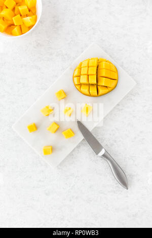 Mango cubes and cut mango half on white marble chopping board and in a white bowl. Top view. Stock Photo