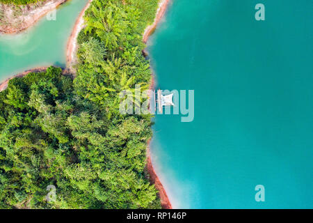 (View from above) Stunning aerial view of a a green coast of a tropical island with a traditional fishing boat in Nam Ngum Reservoir. Stock Photo