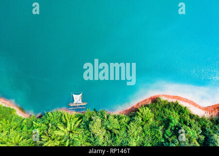 (View from above) Stunning aerial view of a a green coast of a tropical island with a traditional fishing boat in Nam Ngum Reservoir. Stock Photo