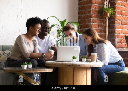 Diverse friends sitting in cafe watching funny videos using computer Stock Photo
