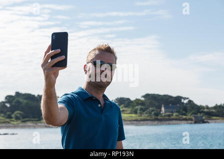 Man taking a selfie with a smartphone at the lakeside Stock Photo
