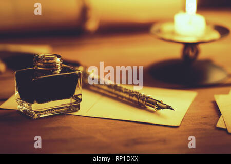 vintage quill pen and inkwell on wooden table in candlelight Stock Photo