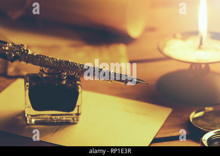 old quill pen and inkwell on brown wooden table with candle Stock Photo