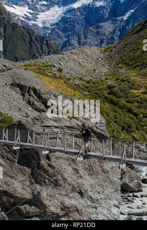 Woman passing a suspension bridge over a glacier river in Mount Cook area in New Zealand Stock Photo