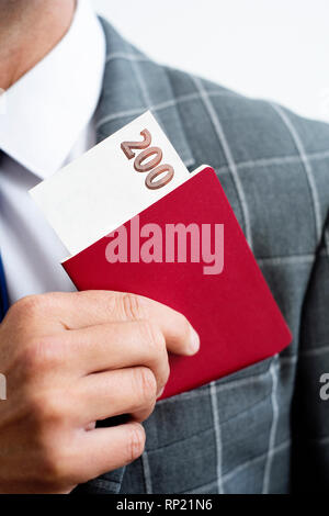 closeup of a young caucasian businessman, wearing an elegant gray suit, taking in or taking off his passport, with a 200 hundred banknote in it, from  Stock Photo