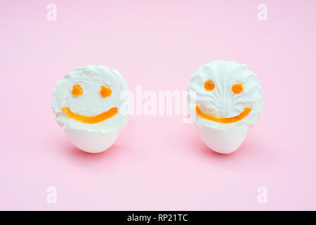 two marshmallows fluff with eyes and smiles from carrots. Funny face in an egg-shell on a pink background. isolated Stock Photo
