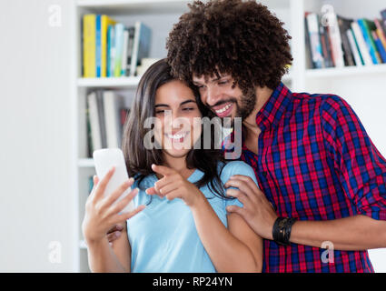Laughing hipster love couple looking at mobile phone indoors at home Stock Photo