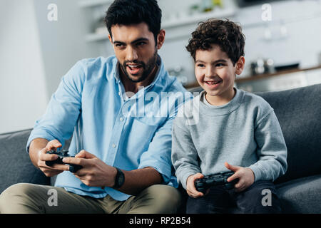 cheerful latin father and son playing video game at home Stock Photo
