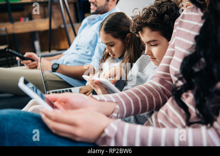 selective focus of kids using gadgets near father and mother at home Stock Photo