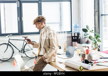 handsome architect using smartphone near table with blueprints in loft office Stock Photo