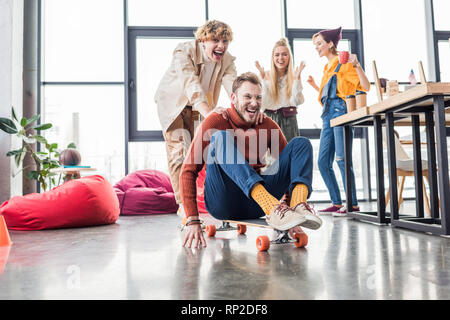 smiling casual business colleagues having fun and riding skateboard in loft office Stock Photo