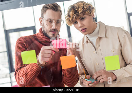 handsome casual businessmen putting colorful sticky notes on glass window in office Stock Photo