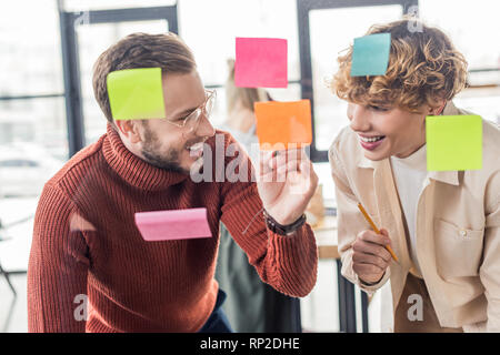 selective focus of handsome casual businessmen putting colorful sticky notes on glass window in office Stock Photo