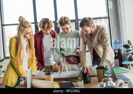 concentrated group of female and male architects working on blueprint at desk in loft office Stock Photo