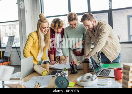 group of female and male architects working on blueprint at desk with laptops in loft office Stock Photo