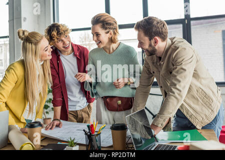 happy group of female and male architects working on blueprint at desk in loft office Stock Photo