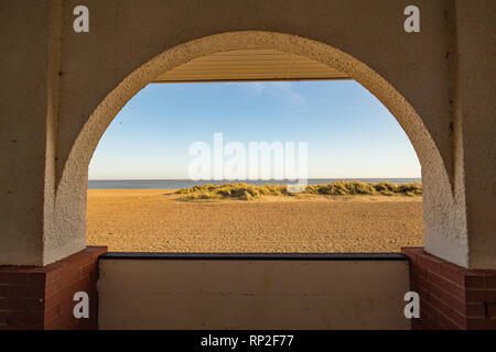 Looking through the arch towards the beach, sand dunes and the blue sea beyond Stock Photo