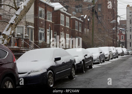 Jersey City, USA. 20th February, 2019. Accumulated fresh snow on a line of similar-looking cars in front of buildings on Britton Street in Jersey City, New Jersey, during a winter afternoon snowfall in February. Except for the odd one out — the rather unsnowy maroon SUV (sports utility vehicle) at the front of the line. Kay Howell/Alamy Live News Stock Photo