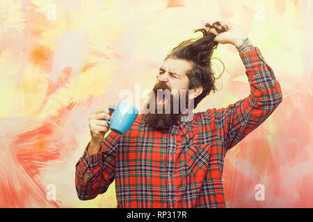 Crying bearded man pulling stylish fringe hair with blue cup Stock Photo