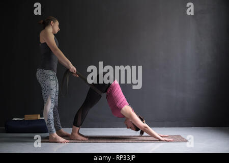 Yoga teacher or pilates instructor helping young woman to stretch muscles. Stock Photo