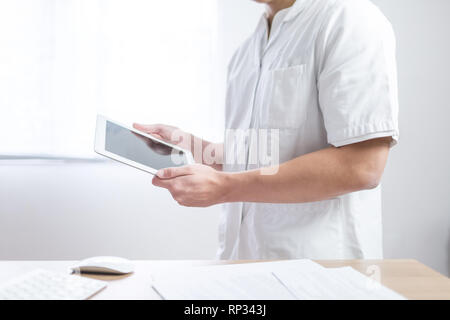Doctor in the uniform using computer tablet next to his office desk in hospital Stock Photo