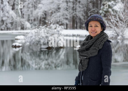 Asian woman bundled up with scarf and hat standing in front of pond Stock Photo