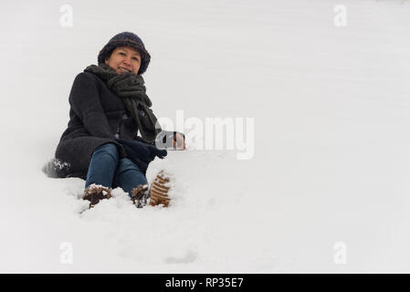 Asian woman in hat and coat laying in snow Stock Photo