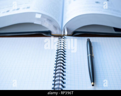 empty student notebook squared with pen and blurred book with lot of bookmarks as background. closeup image depict education process Stock Photo