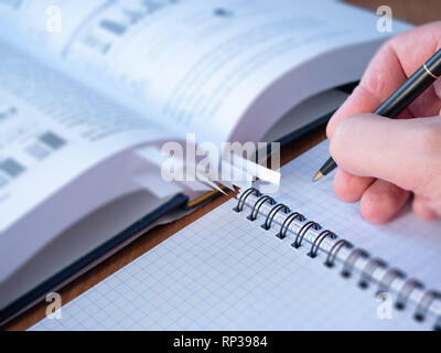 selective focus image of witer or student hand with pen above blank page of binder textbook. blurred opened book on background Stock Photo