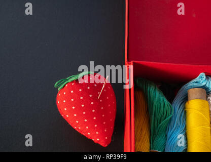 little needle pod with box full of colorful vivid treads. craft hobby handmade concept. low key image on black background Stock Photo