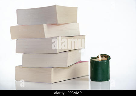 Composition of green burning candle and pile of books against white background Stock Photo