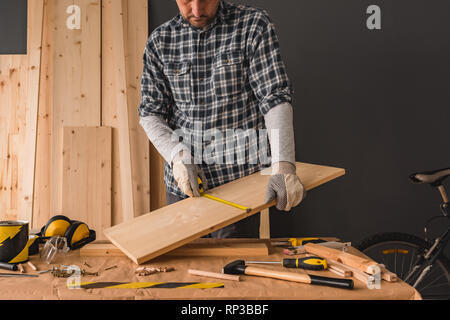 Carpenter is measuring pine wood plank with tape measure for woodwork project in workshop Stock Photo