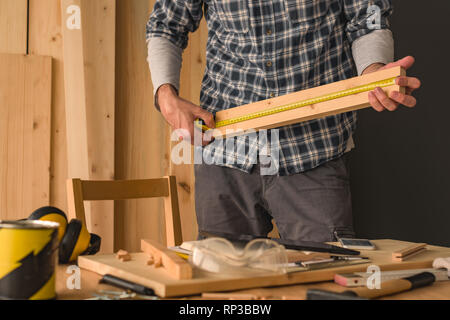 Carpenter is measuring pine wood plank with tape measure for woodwork project in workshop Stock Photo