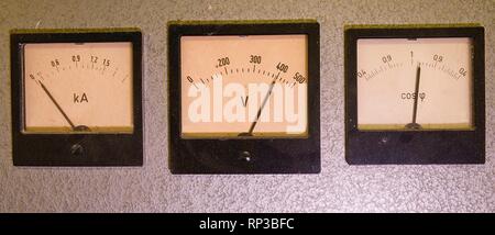 Three old analog instruments - Power factor meter, voltmeter and ampere meter isolated on grey background. Stock Photo