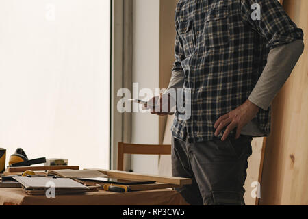 Carpenter is using smartphone for  texting in woodwork workshop Stock Photo