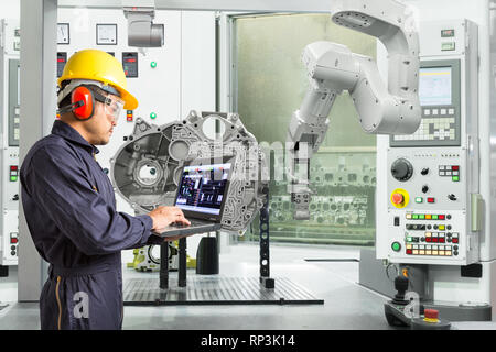 Engineer using laptop computer control automatic robotic hand with CNC machine in automotive industry, Smart factory concept Stock Photo