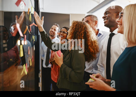 Young businesswoman talking with her diverse team during a brainstorming session with sticky notes in a modern office Stock Photo