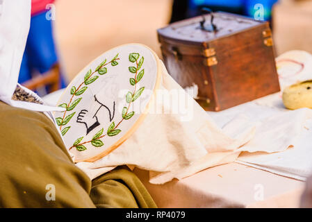 Young woman seamstress sewing a simple drawing, disguised as medieval in a traditional craft children's exhibition. Stock Photo