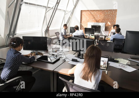 Diverse millennial employees male female sitting at desk using laptops working in coworking open space modern light room with panoramic windows. Multi Stock Photo