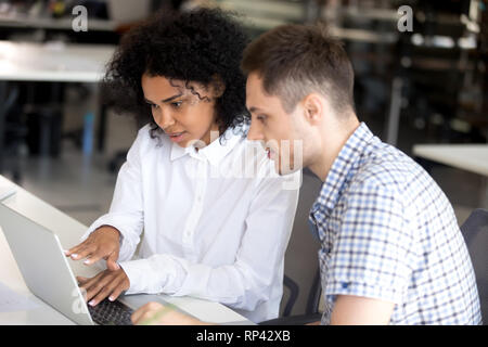 Diverse students studying together looking at computer screen. Black african american team leader or coach helps new employee intern man, mentor expla Stock Photo