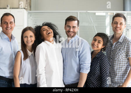 Millennial happy multi ethnic employees standing in row posing looking at camera. Six smiling successful office workers feels motivated ready for succ Stock Photo