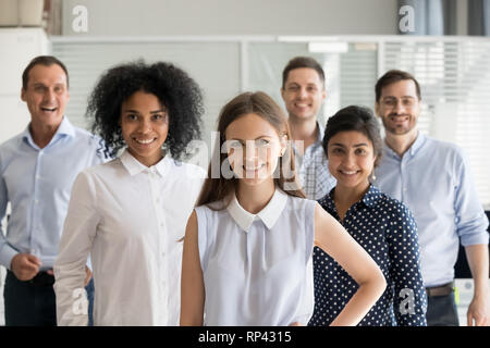 Diverse team headed by successful attractive leader woman standing together in a row indoors. Office workers caucasian indian and african nationality Stock Photo