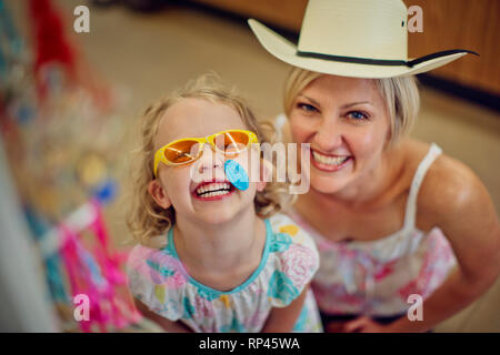 Portrait of a happy young girl and her mother playing dress-up in a beachwear store. Stock Photo