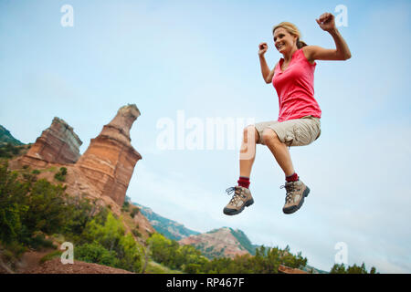 Happy young woman jumps joyfully into the air while on a hiking trip. Stock Photo