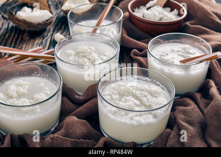 close-up of homemade coconut cocktail of coconut water, coconut milk and cream in the glass cups on a rustic wooden table with ingredients and brown c Stock Photo