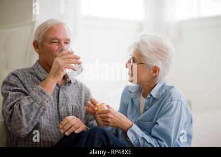 Senior woman holding pill bottle while husband takes a pill Stock Photo