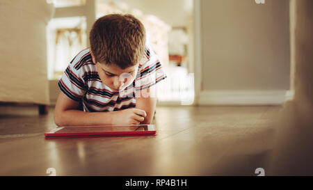 Close up of a boy sitting on floor looking at a tablet pc. Boy using a tablet pc sitting down on floor at home. Stock Photo