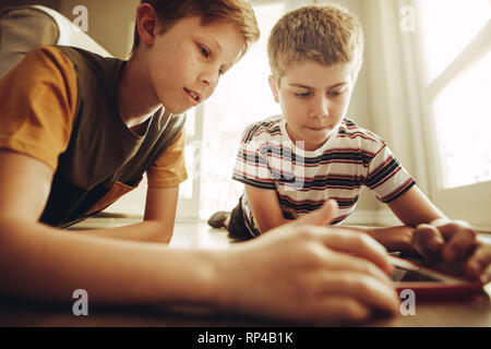 Two boys playing a game on tablet pc with great interest. Kids lying on floor at home using a tablet pc. Stock Photo
