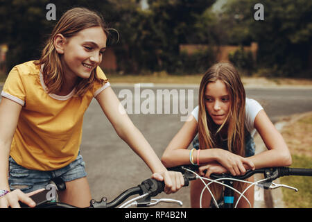 Two cheerful girls riding bicycles outdoors. Girls sitting on bicycles and talking to each other. Stock Photo