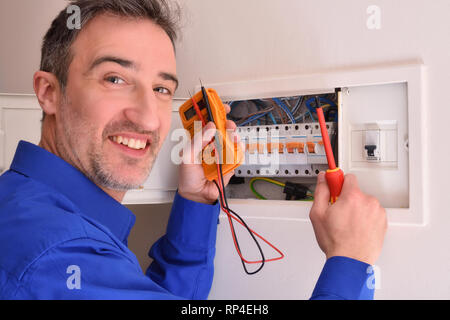 Smiling electrician with tester and screwdriver making repairs in electrical housing box Stock Photo